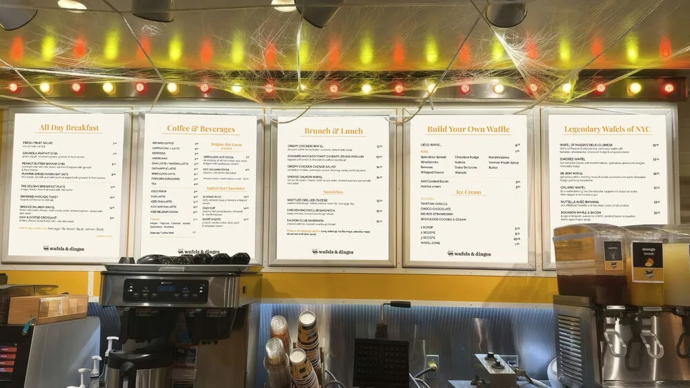 Illuminated menu board panels inside a Wafels & Dinges kiosk, New York City